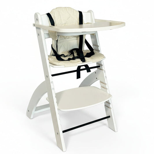 En justerbar høy barnestol i tre, hvit farge, utstyrt med en hvit pute og sikkerhetssele. Den har et avtagbart brett og er vist sammenfelt med fotbrettet ute.