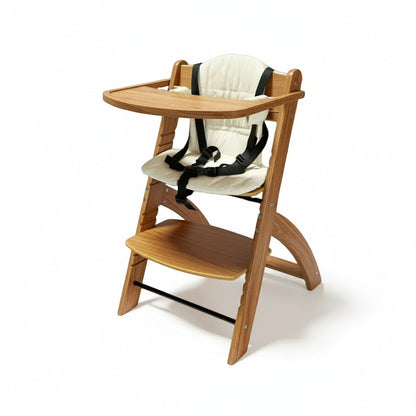 A wooden adjustable high chair with a natural finish, equipped with a white cushion and a safety harness. It has a removable tray and is shown folded with the footrest extended.